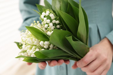 Photo of Woman with beautiful lilies of the valley flowers indoors, closeup