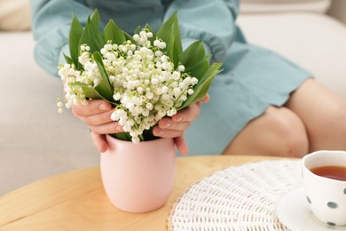 Photo of Woman with beautiful lilies of the valley flowers on sofa at table indoors, closeup