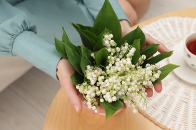 Photo of Woman with beautiful lilies of the valley flowers on sofa at table indoors, closeup