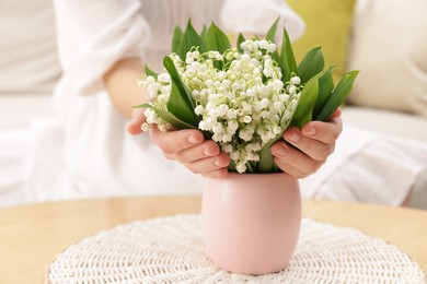 Photo of Woman with beautiful lilies of the valley flowers on sofa at table indoors, closeup