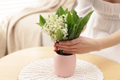 Photo of Woman with beautiful lilies of the valley flowers on sofa at table indoors, closeup