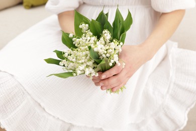 Photo of Woman with beautiful lilies of the valley flowers on sofa indoors, closeup