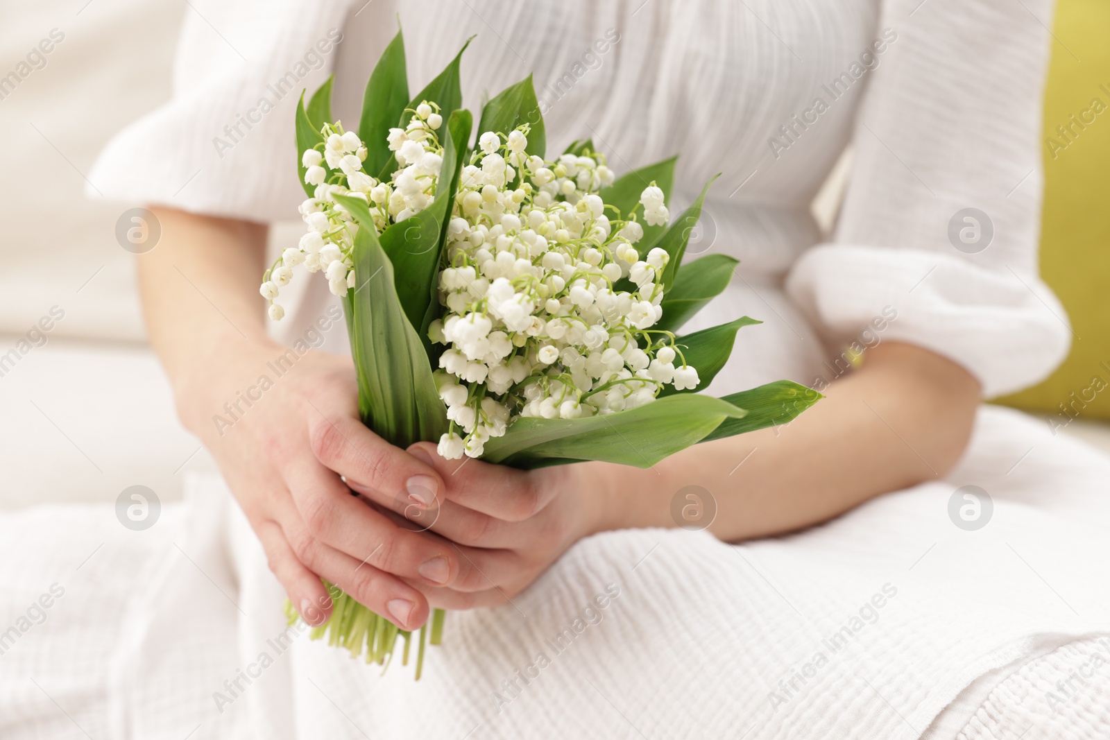 Woman with beautiful lilies of the valley flowers on sofa indoors, closeup Photo of Woman with beautiful lilies of the valley flowers on sofa indoors, closeup