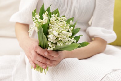 Photo of Woman with beautiful lilies of the valley flowers on sofa indoors, closeup