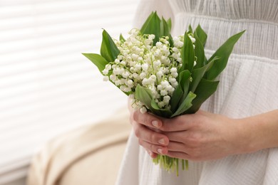 Photo of Woman with beautiful lilies of the valley flowers indoors, closeup