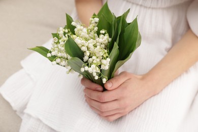 Photo of Woman with beautiful lilies of the valley flowers indoors, closeup
