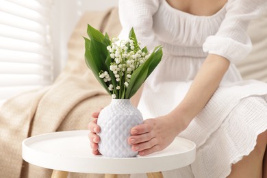 Photo of Woman with beautiful lilies of the valley flowers on sofa at table indoors, closeup