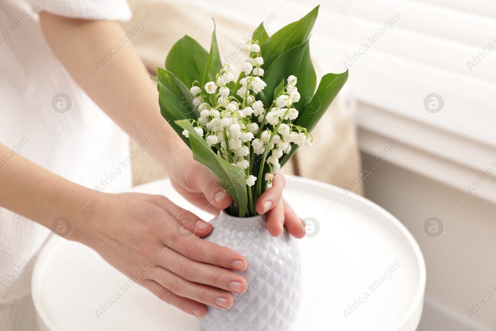 Woman with beautiful lilies of the valley flowers on sofa at table indoors, closeup Photo of Woman with beautiful lilies of the valley flowers on sofa at table indoors, closeup
