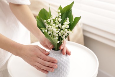 Photo of Woman with beautiful lilies of the valley flowers on sofa at table indoors, closeup