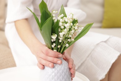 Photo of Woman with beautiful lilies of the valley flowers on sofa at table indoors, closeup