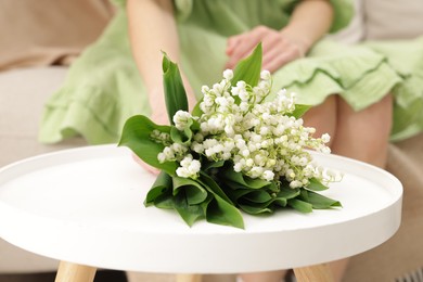 Photo of Woman with beautiful lilies of the valley flowers on sofa at table indoors, closeup