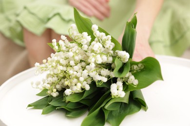 Photo of Woman with beautiful lilies of the valley flowers on sofa at table indoors, closeup