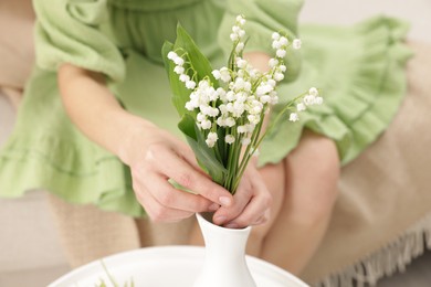 Photo of Woman with beautiful lilies of the valley flowers on sofa at table indoors, closeup