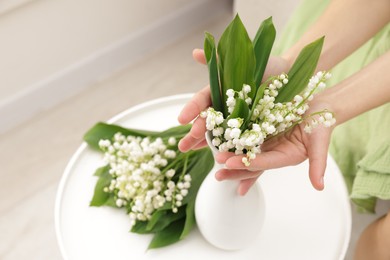 Photo of Woman with beautiful lilies of the valley flowers on sofa at table indoors, closeup