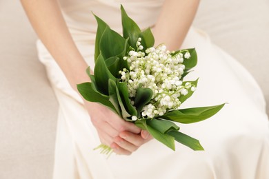 Photo of Woman with beautiful lilies of the valley flowers on sofa indoors, closeup