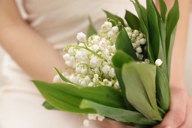 Photo of Woman with beautiful lilies of the valley flowers indoors, closeup