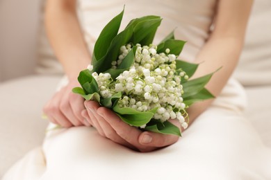 Photo of Woman with beautiful lilies of the valley flowers on sofa indoors, closeup
