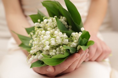Photo of Woman with beautiful lilies of the valley flowers indoors, closeup