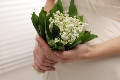 Photo of Woman with beautiful lilies of the valley flowers indoors, closeup