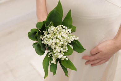 Photo of Woman with beautiful lilies of the valley flowers indoors, closeup