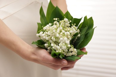 Photo of Woman with beautiful lilies of the valley flowers indoors, closeup