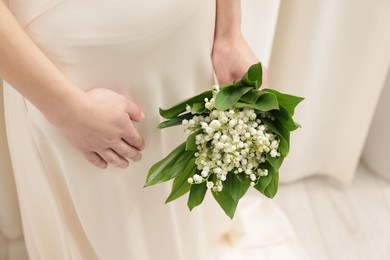 Photo of Woman with beautiful lilies of the valley flowers indoors, closeup