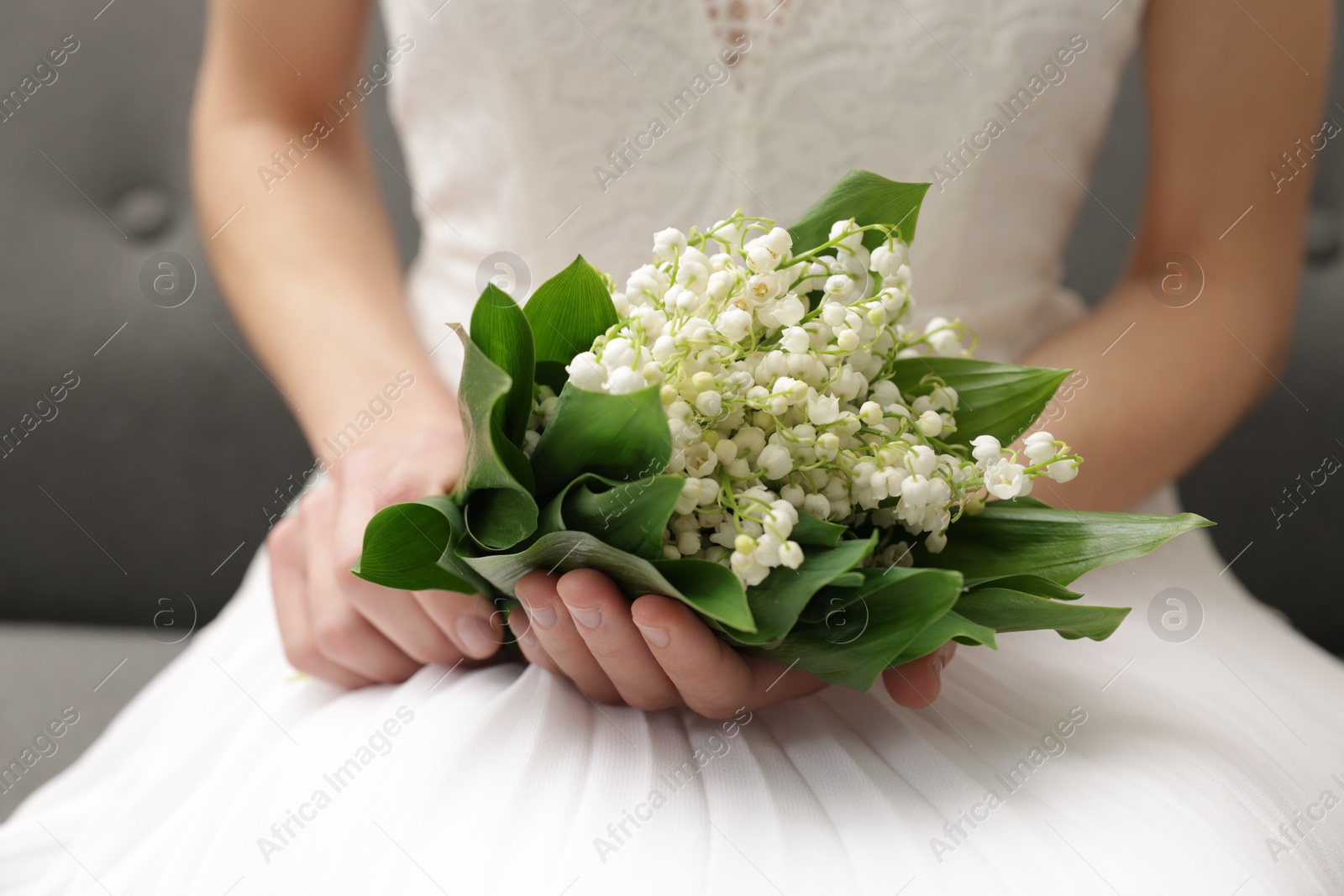 Bride with bouquet of beautiful lilies of the valley on sofa indoors, closeup Photo of Bride with bouquet of beautiful lilies of the valley on sofa indoors, closeup