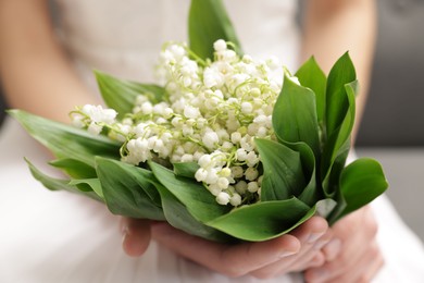 Photo of Bride with bouquet of beautiful lilies of the valley on sofa indoors, closeup