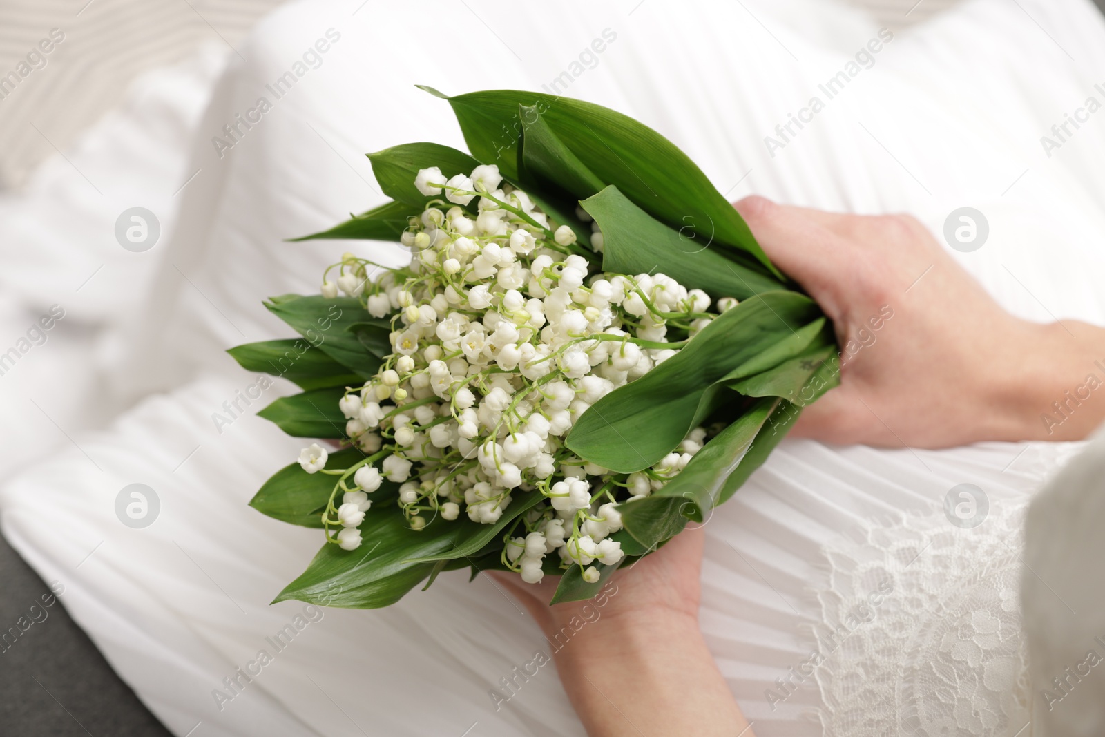 Bride with bouquet of beautiful lilies of the valley on sofa indoors, closeup Photo of Bride with bouquet of beautiful lilies of the valley on sofa indoors, closeup
