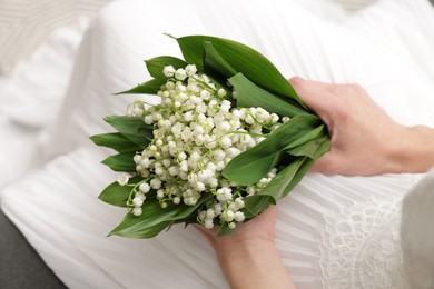 Photo of Bride with bouquet of beautiful lilies of the valley on sofa indoors, closeup