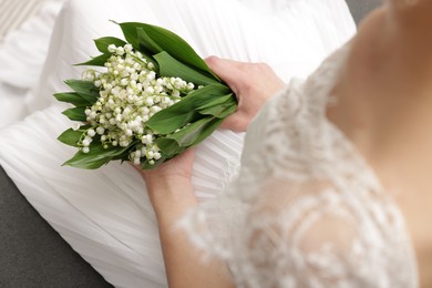 Photo of Bride with bouquet of beautiful lilies of the valley on sofa indoors, closeup