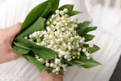Photo of Bride with bouquet of beautiful lilies of the valley on sofa indoors, closeup