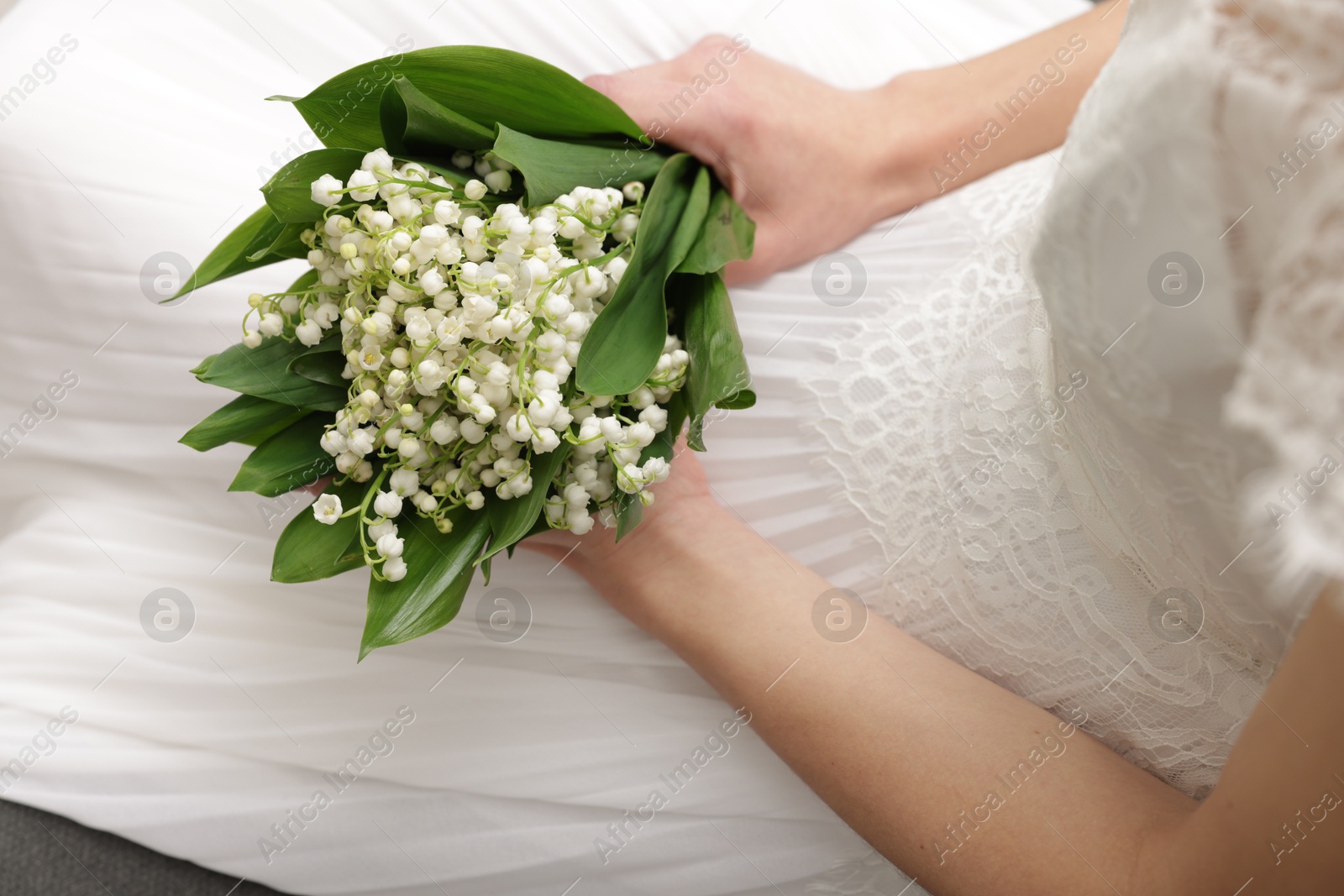 Bride with bouquet of beautiful lilies of the valley on sofa indoors, closeup Photo of Bride with bouquet of beautiful lilies of the valley on sofa indoors, closeup