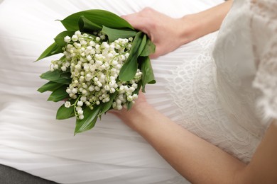 Photo of Bride with bouquet of beautiful lilies of the valley on sofa indoors, closeup