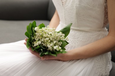 Photo of Bride with bouquet of beautiful lilies of the valley on sofa indoors, closeup