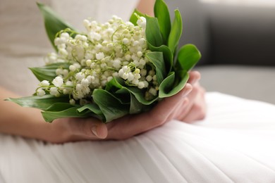 Photo of Bride with bouquet of beautiful lilies of the valley on sofa indoors, closeup