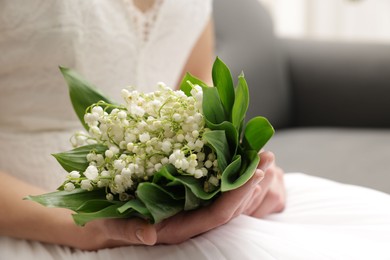 Photo of Bride with bouquet of beautiful lilies of the valley on sofa indoors, closeup