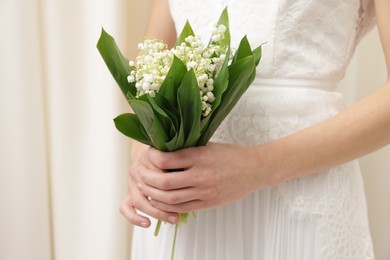 Photo of Bride with bouquet of beautiful lilies of the valley indoors, closeup