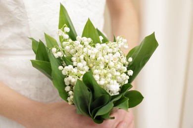 Photo of Bride with bouquet of beautiful lilies of the valley indoors, closeup