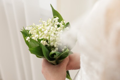 Photo of Bride with bouquet of beautiful lilies of the valley indoors, closeup