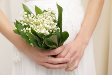 Photo of Bride with bouquet of beautiful lilies of the valley indoors, closeup
