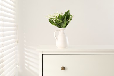 Photo of Beautiful lilies of the valley flowers in vase on chest of drawers