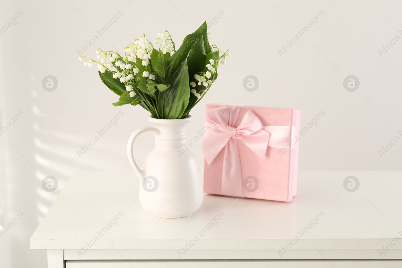 Beautiful lilies of the valley flowers and gift on white table Photo of Beautiful lilies of the valley flowers and gift on white table