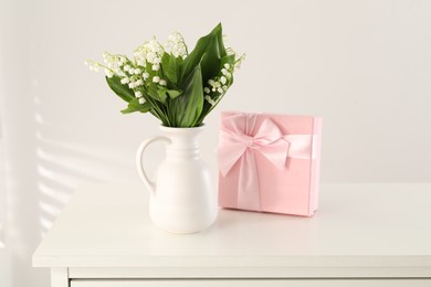 Photo of Beautiful lilies of the valley flowers and gift on white table
