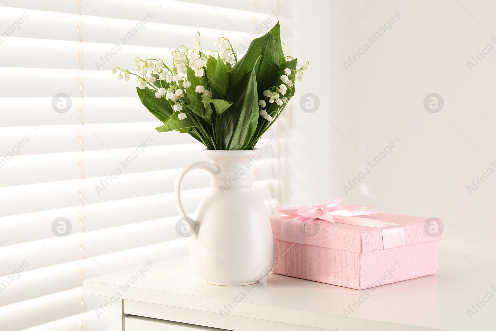 Beautiful lilies of the valley flowers and gift on white table indoors Photo of Beautiful lilies of the valley flowers and gift on white table indoors