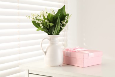 Photo of Beautiful lilies of the valley flowers and gift on white table indoors