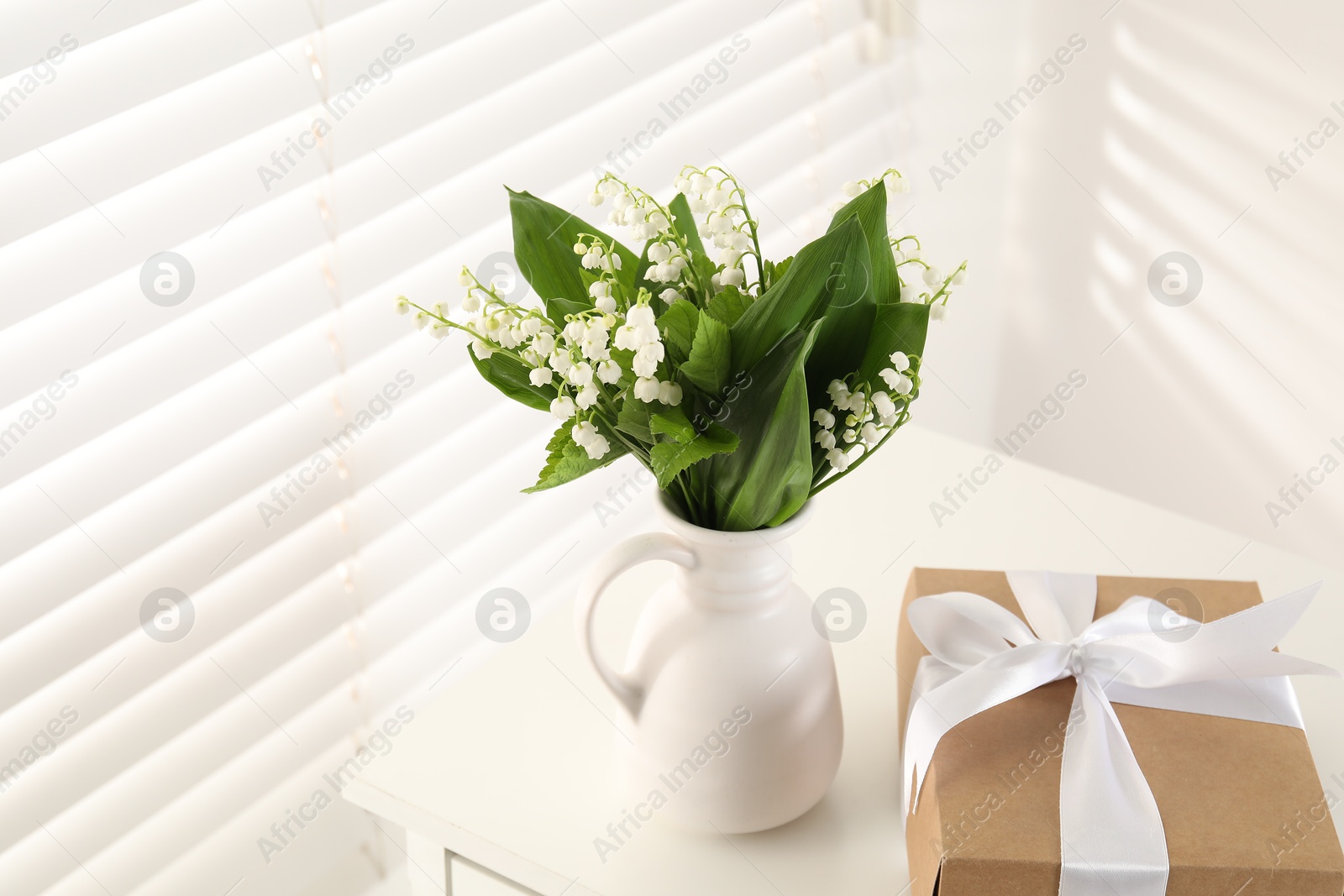 Beautiful lilies of the valley flowers and gift on white table indoors Photo of Beautiful lilies of the valley flowers and gift on white table indoors
