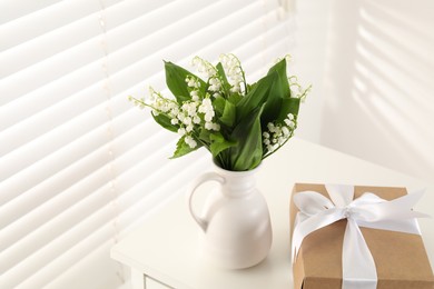 Photo of Beautiful lilies of the valley flowers and gift on white table indoors
