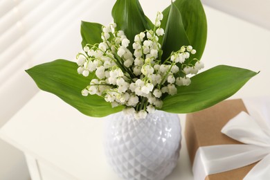 Photo of Beautiful lilies of the valley flowers and gift on table indoors, closeup