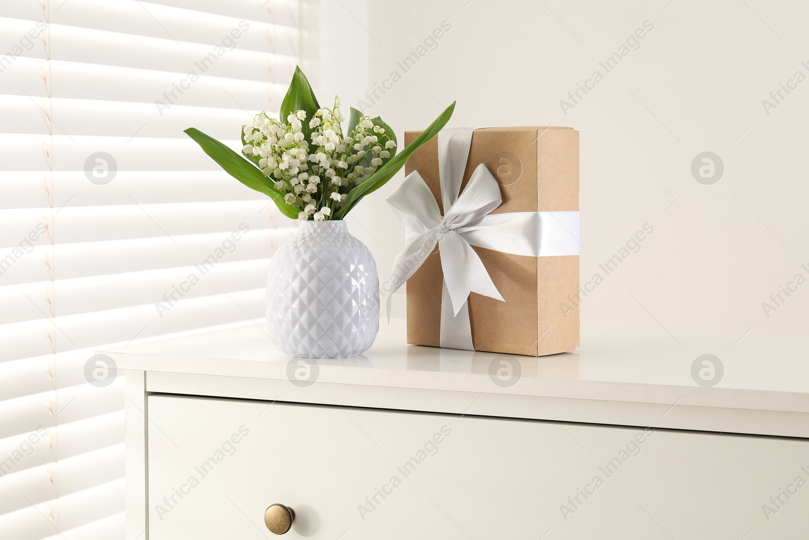 Beautiful lilies of the valley flowers and gift on white table indoors Photo of Beautiful lilies of the valley flowers and gift on white table indoors